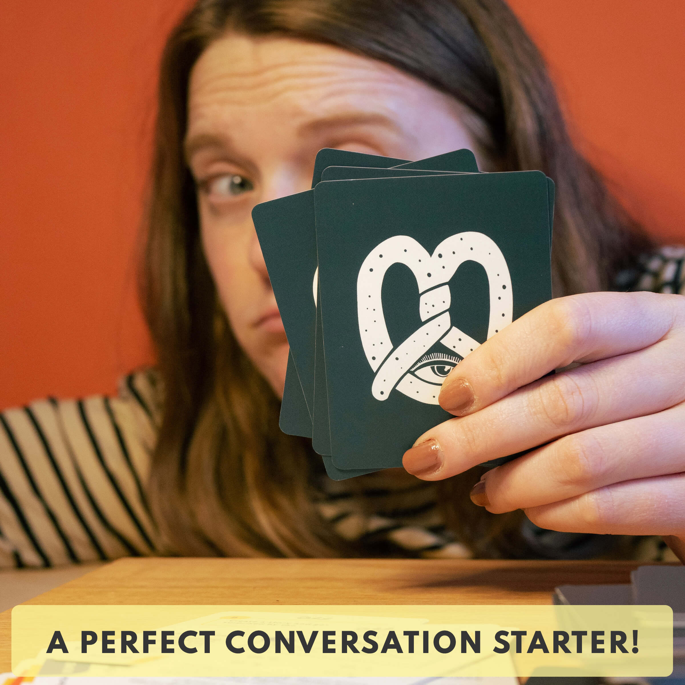 Person holding playing cards with a heart and eye design, against an orange background.