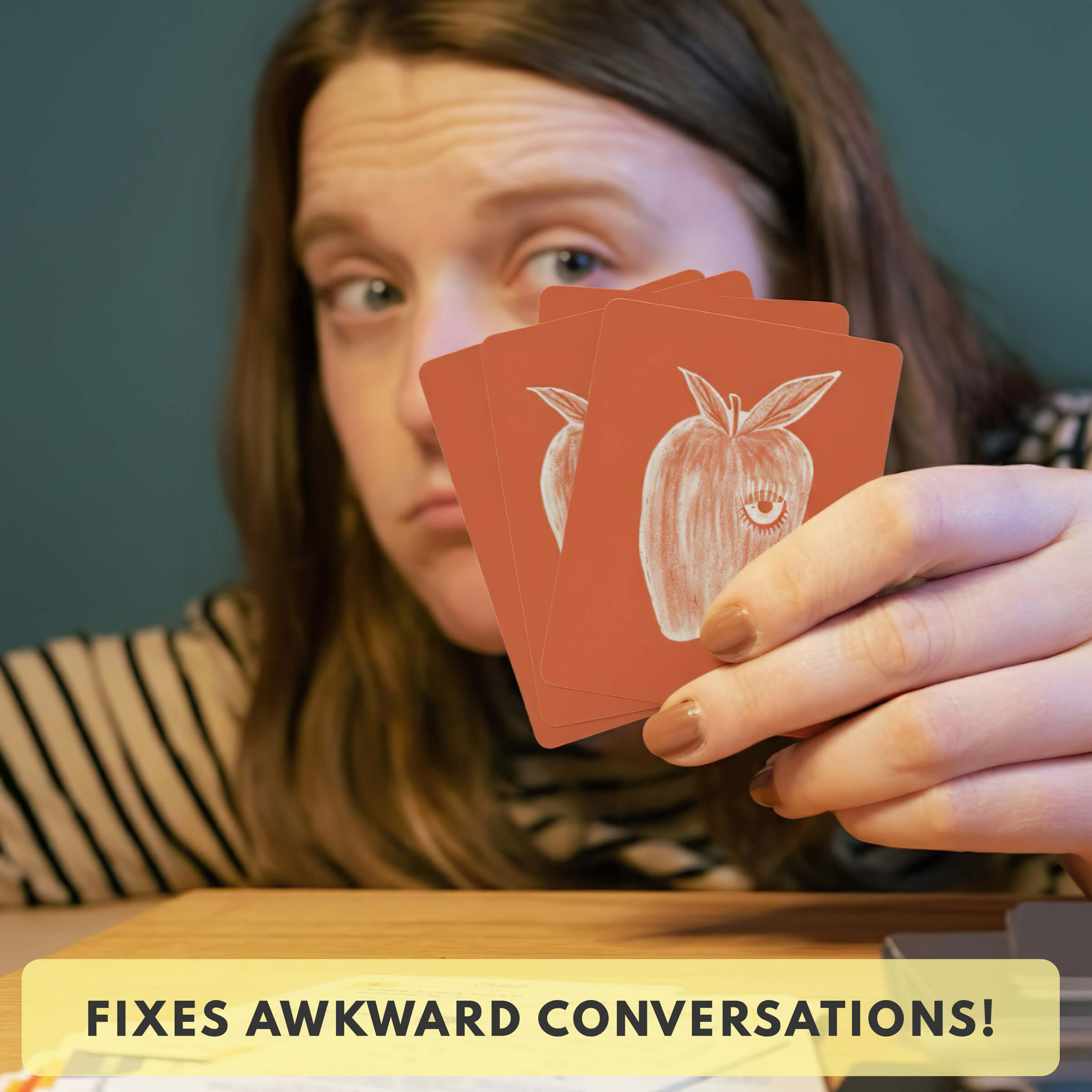 Person holding playing cards with an apple design, text 'FIXES AWKWARD CONVERSATIONS!' at the bottom.
