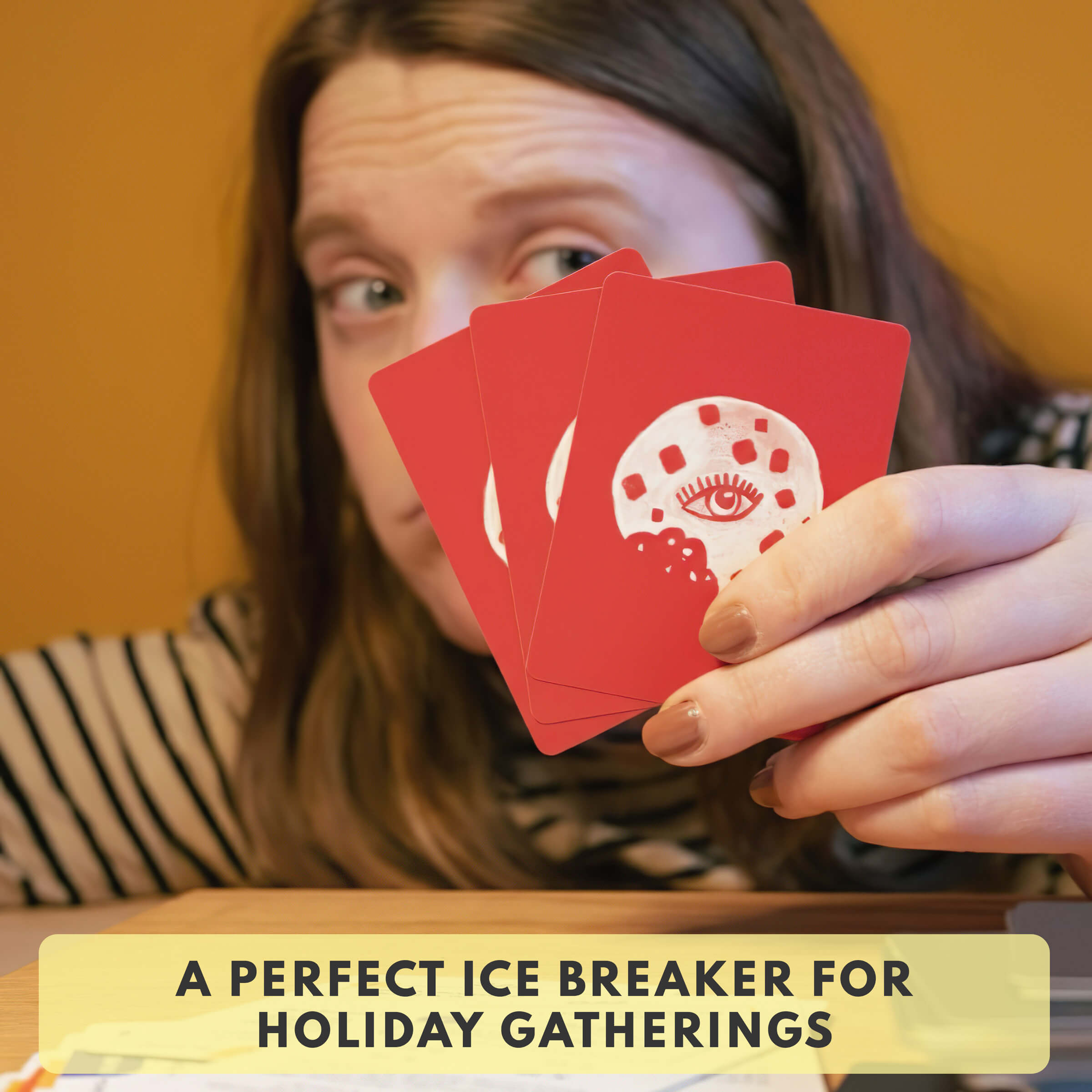 Person holding red cards with a face design, text 'A PERFECT ICE BREAKER FOR HOLIDAY GATHERINGS' below.