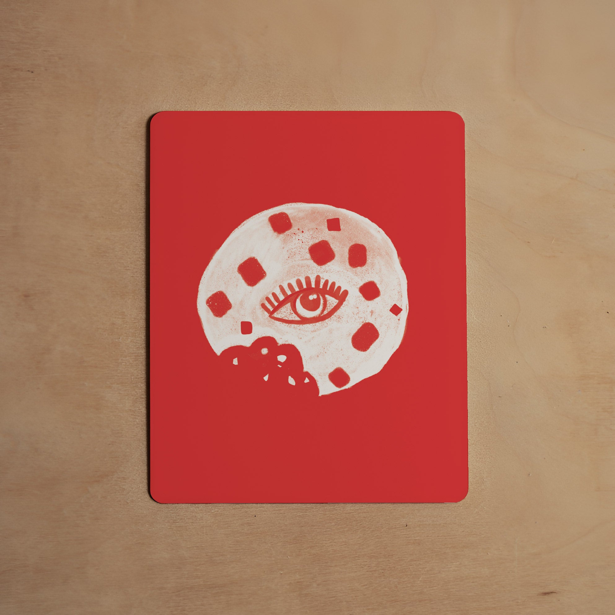 Red coaster with white abstract design featuring an eye on a wooden surface