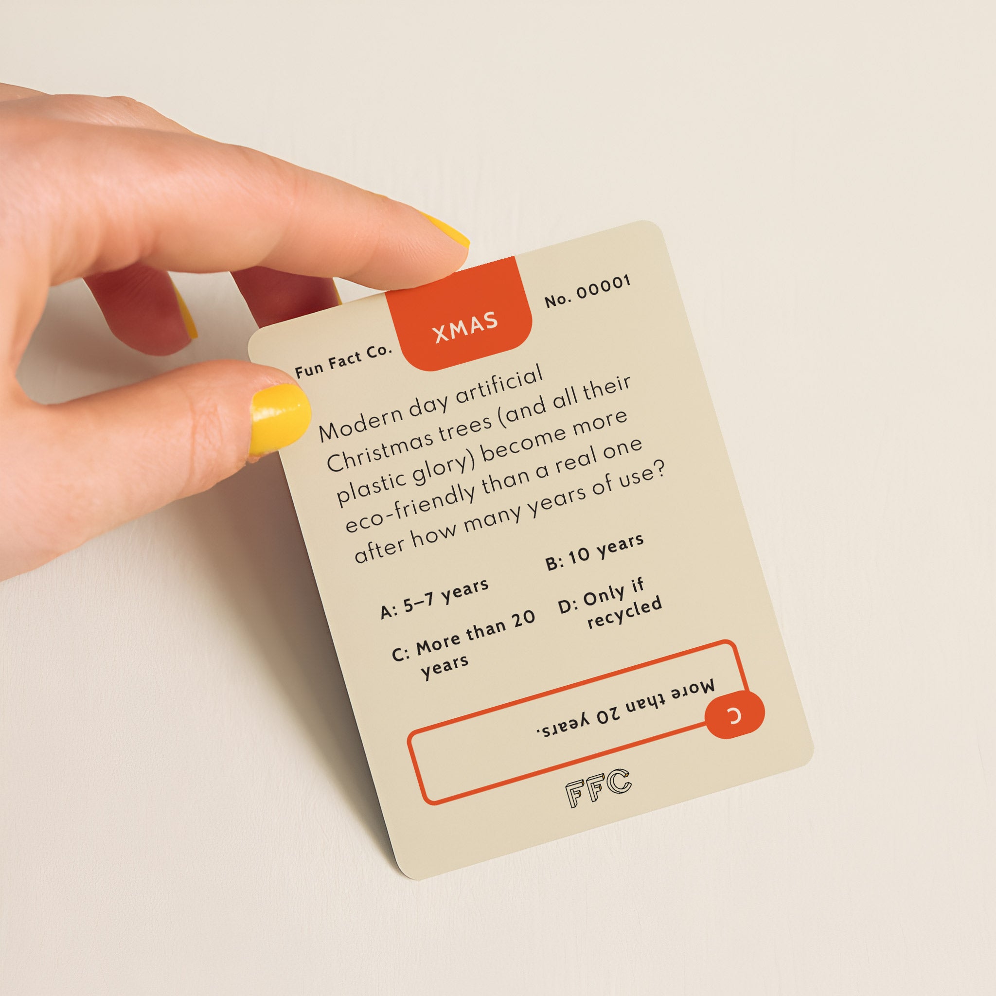Hand holding a card with text about modern Christmas trees and eco-friendliness on a beige background