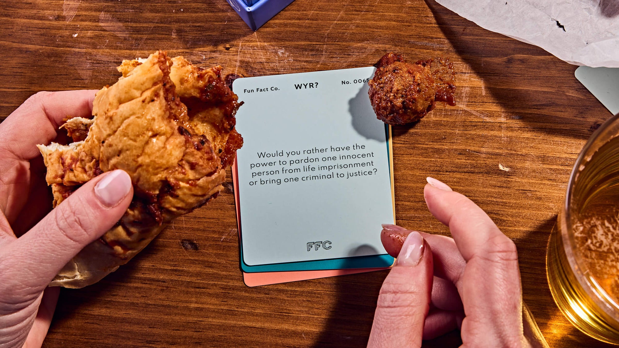 Person holding fried chicken and a card on a wooden table with a glass of beer.