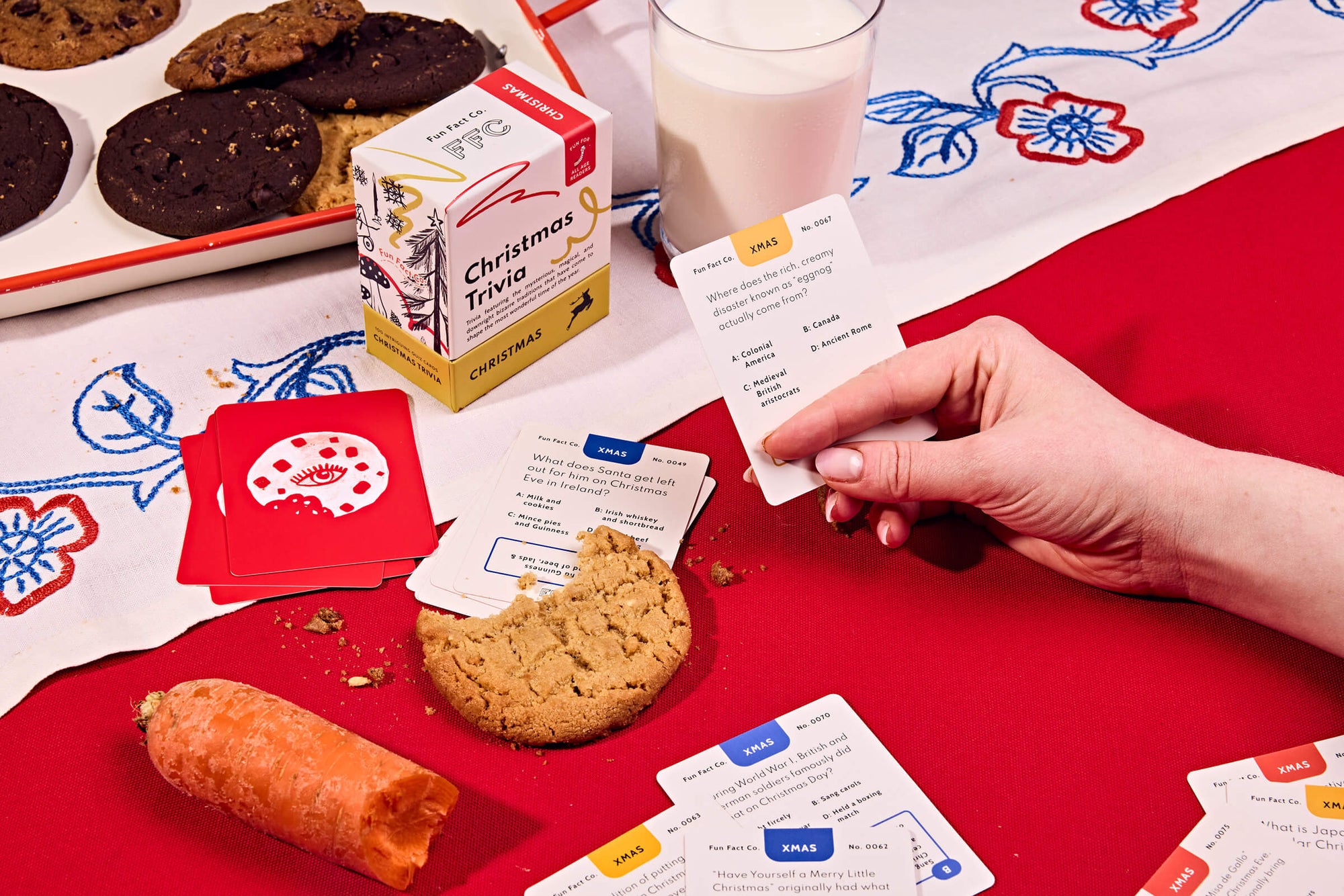 Person playing a card game with cookies and a glass of milk on a red tablecloth.